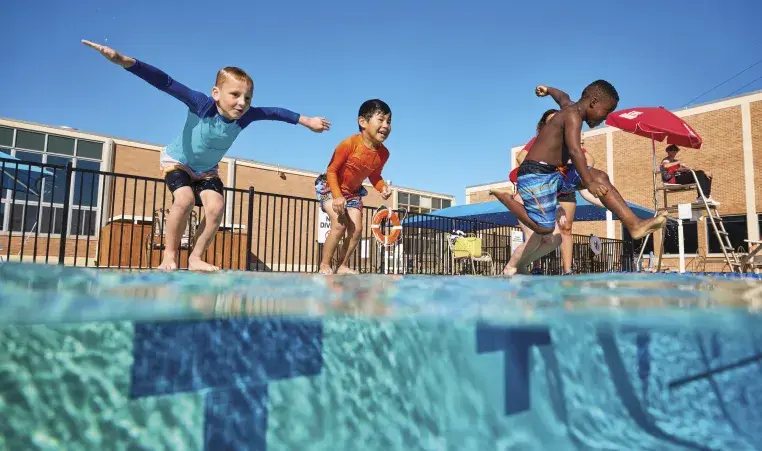 three children jumping into an outdoor pool