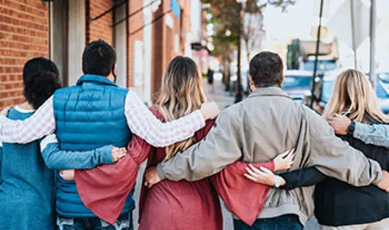 A group of friends locks arms outside a brick building